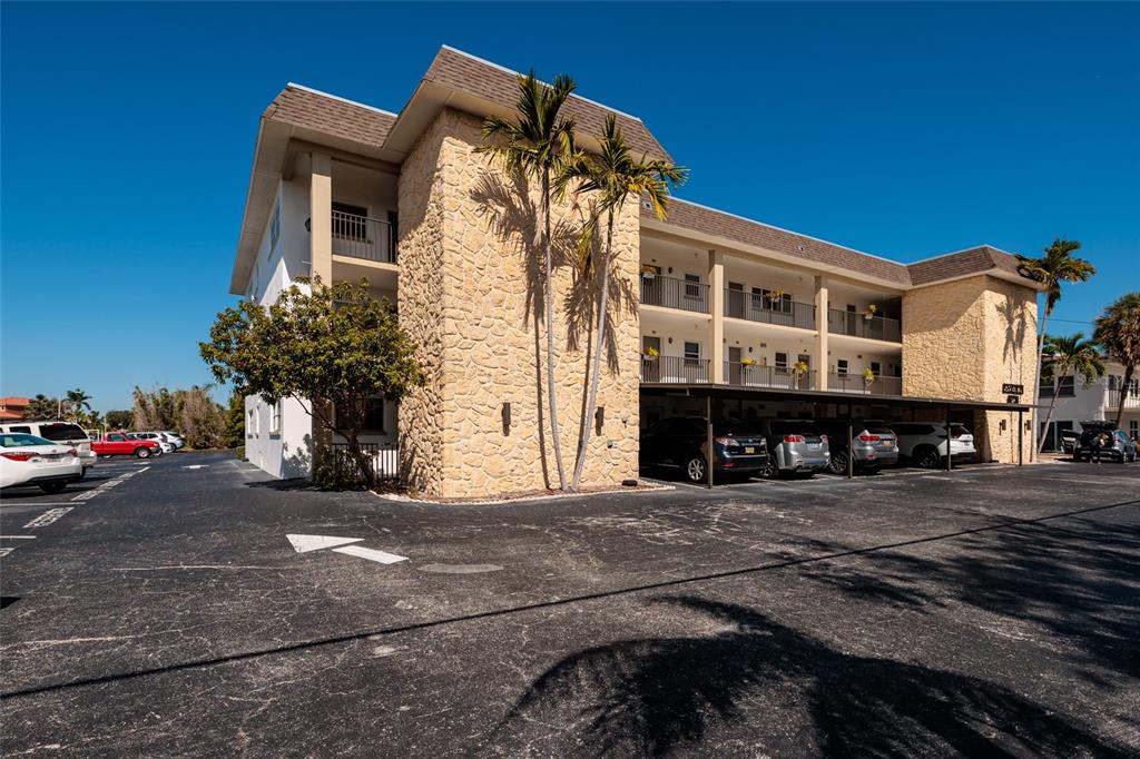 A multi-story apartment building features stone facade accents, covered parking, and palm trees — 3789 46TH AVENUE S UNIT 101, ST PETERSBURG, FL