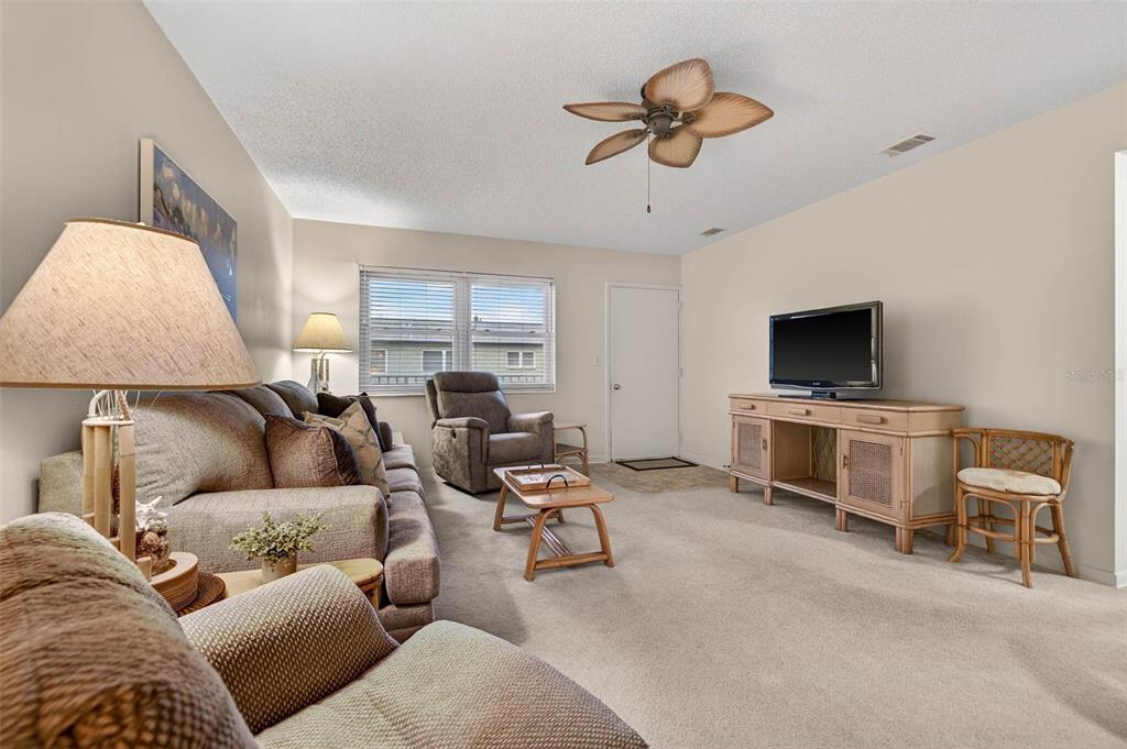 A living room features a sofa, recliner, television on a wooden stand, and ceiling fan — 5267 81ST STREET N UNIT 18, ST PETERSBURG, FL