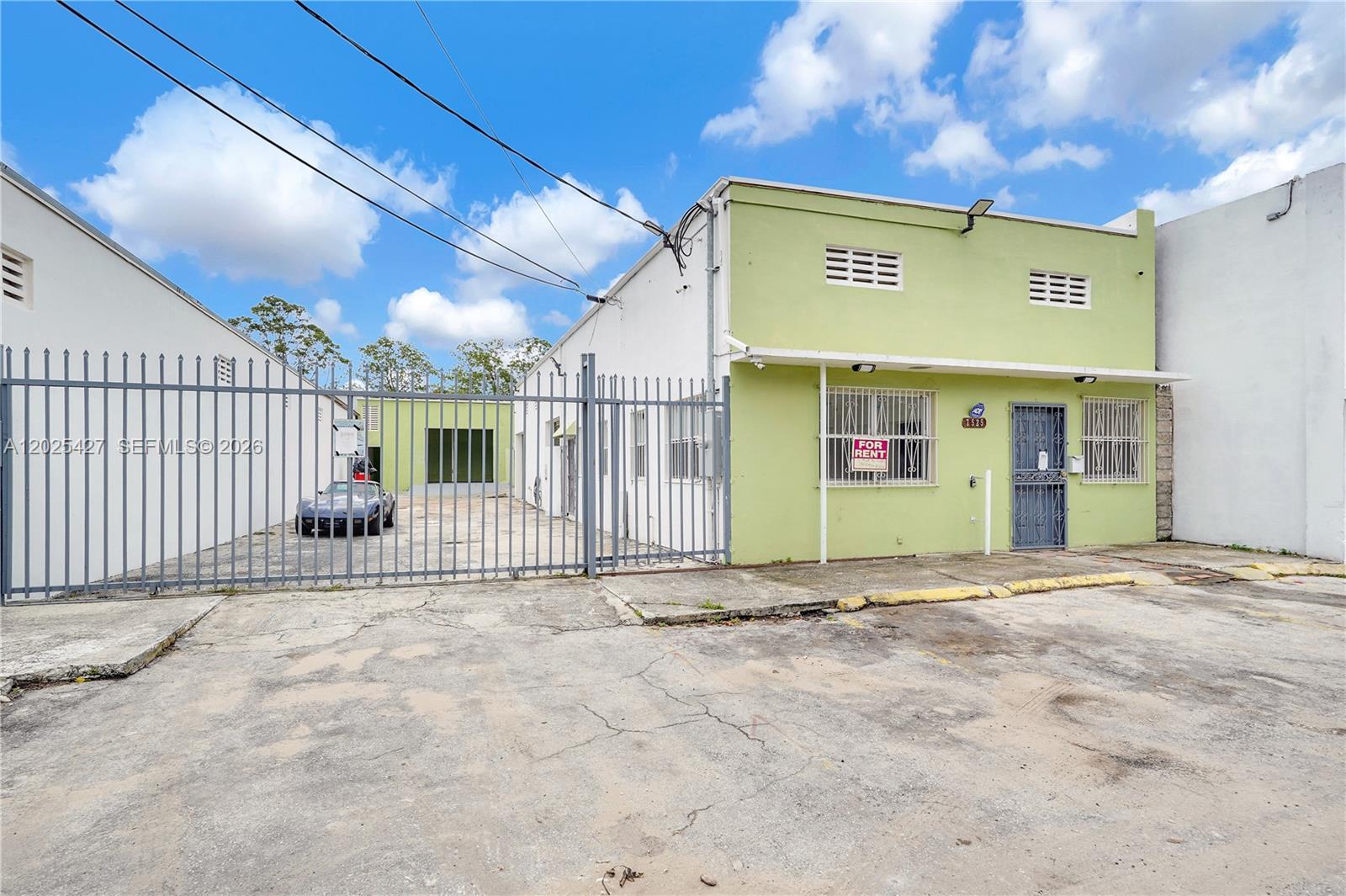 A light green commercial building features a gated parking area and a for rent sign — 7525 NE 3rd Pl, Miami FL 33138, MIAMI, FL