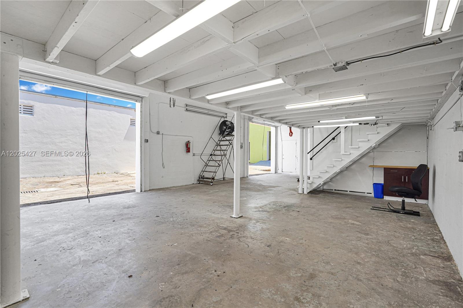 An industrial-style space features a concrete floor, exposed white ceiling beams, and a staircase — 7525 NE 3rd Pl, Miami FL 33138, MIAMI, FL