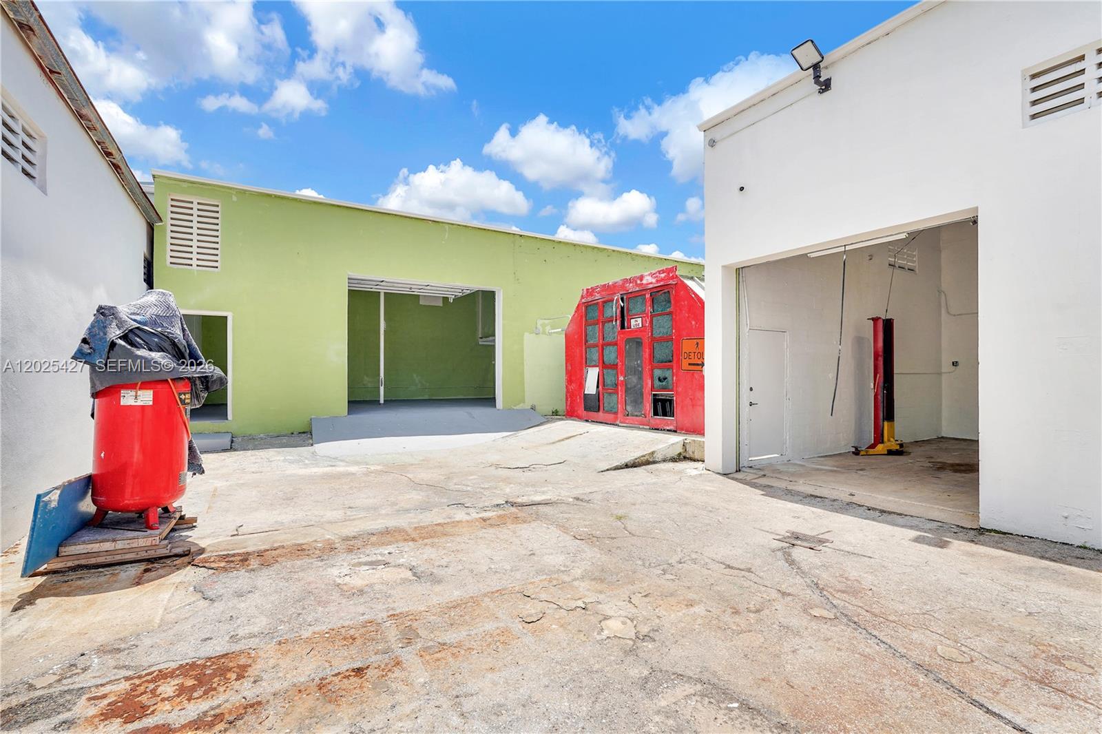An outdoor concrete lot features a red air compressor, a green building, and white bays — 7525 NE 3rd Pl, Miami FL 33138, MIAMI, FL