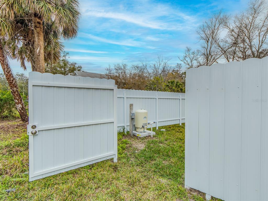 A white vinyl fence gate opens to reveal a well pump on a concrete pad — 3837 STREAMSIDE LANE, NEW PORT RICHEY, FL