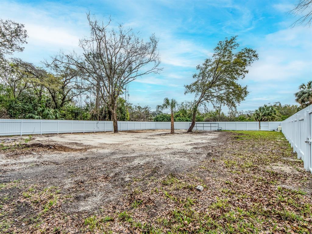 A large, cleared backyard features sandy ground, several trees, and a white vinyl privacy fence — 3837 STREAMSIDE LANE, NEW PORT RICHEY, FL