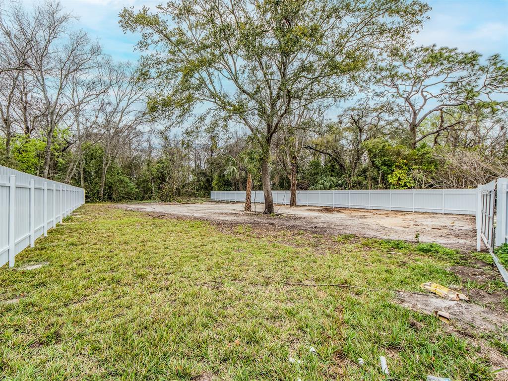 A fenced backyard features a grassy area leading to a cleared, sandy plot with trees — 3837 STREAMSIDE LANE, NEW PORT RICHEY, FL