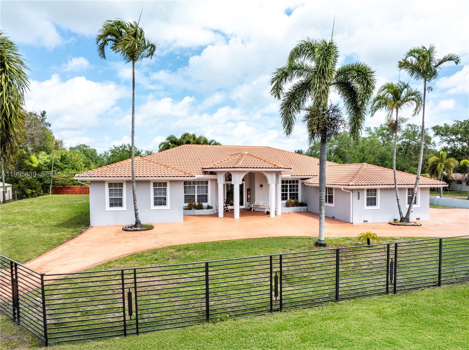 A single-story house with a terracotta tile roof and palm trees sits behind a fence — 5303 SW 111th Ter, Davie FL 33328, DAVIE, FL