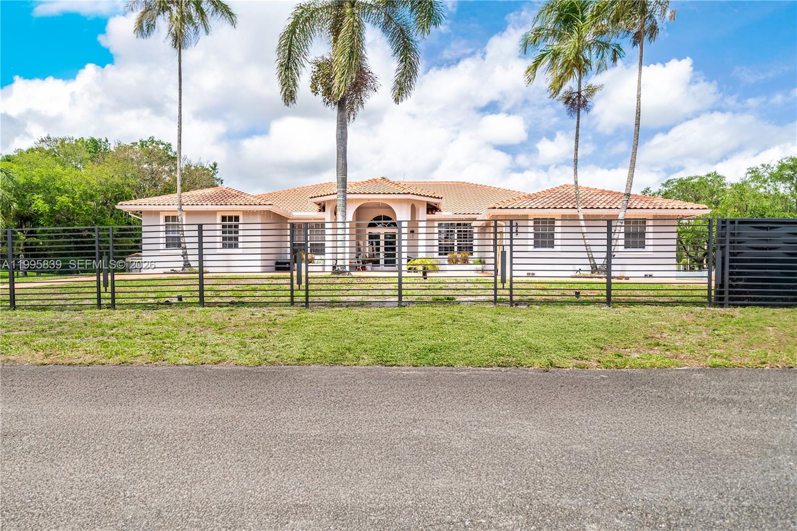 A single-story house with a tiled roof and palm trees sits behind a metal fence — 5303 SW 111th Ter, Davie FL 33328, DAVIE, FL