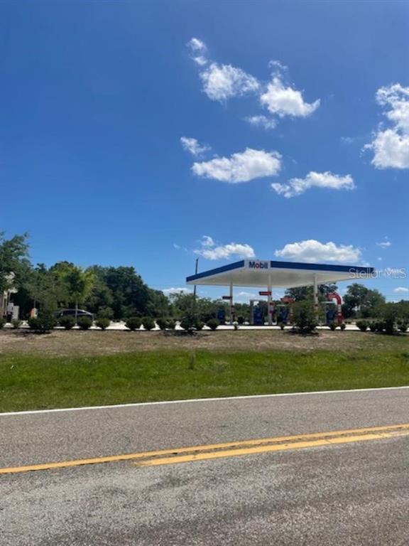 A Mobil gas station with a fuel canopy stands near a road under a blue sky — KISSIMMEE WAY, POINCIANA, FL