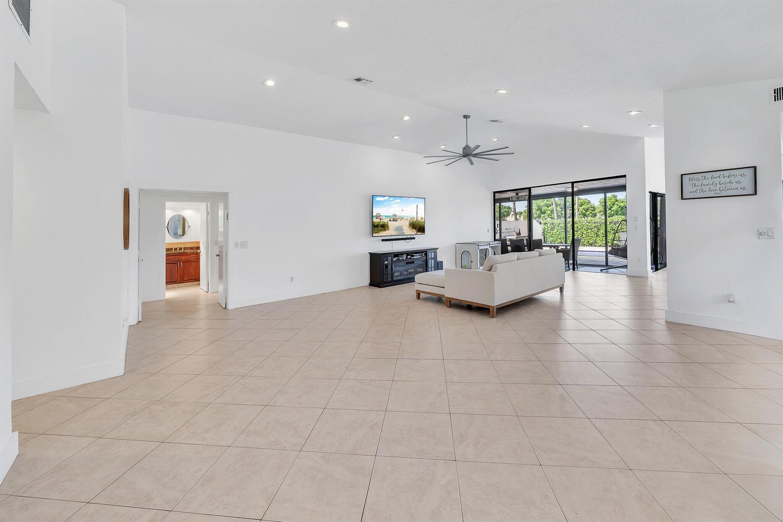 A spacious living room with tile floors, a white sofa, and a wall-mounted television — 10255 Sunset Bend Drive, Boca Raton FL 33428, BOCA RATON, FL
