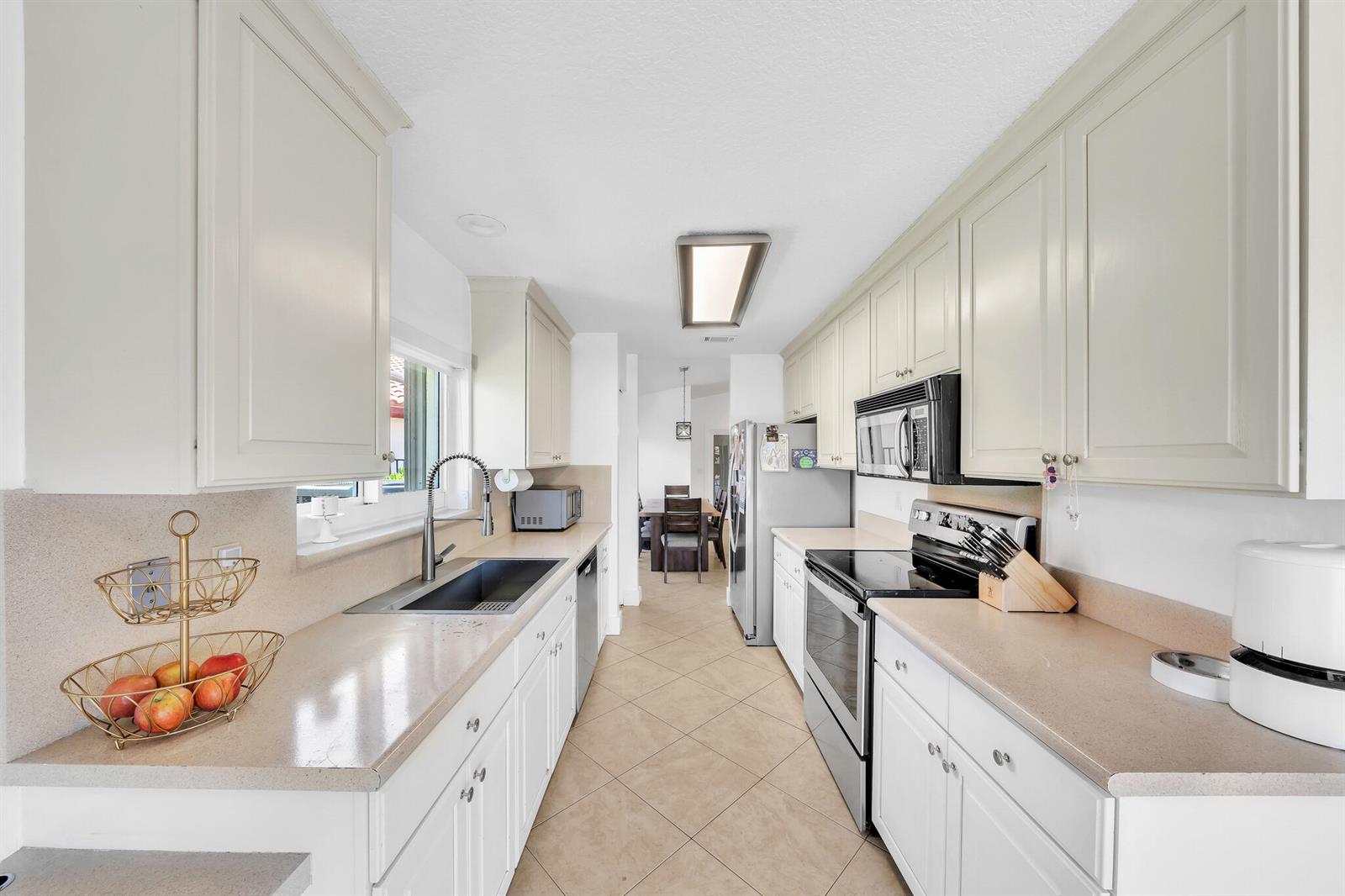 A galley kitchen features white cabinets, beige countertops, stainless steel appliances, and tile flooring — 10255 Sunset Bend Drive, Boca Raton FL 33428, BOCA RATON, FL