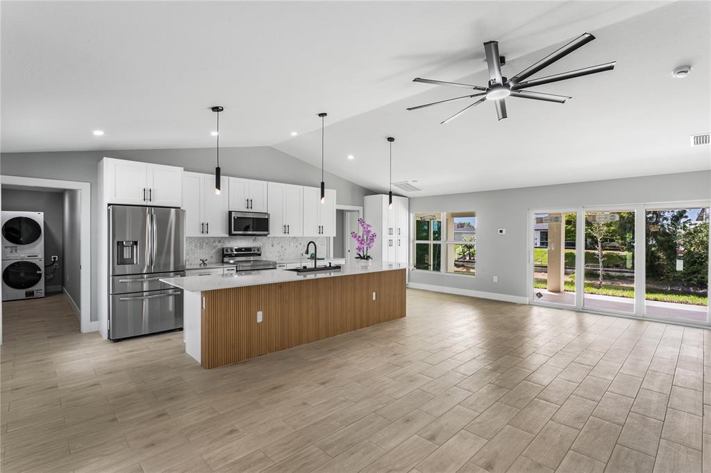 A modern kitchen features white cabinetry, a wood-slatted island, stainless appliances, and light tile flooring — 2210 NW 2ND AVENUE, CAPE CORAL, FL