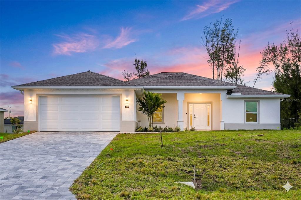 A single-story white stucco house with a two-car garage and a paved driveway at sunset — 2210 NW 2ND AVENUE, CAPE CORAL, FL
