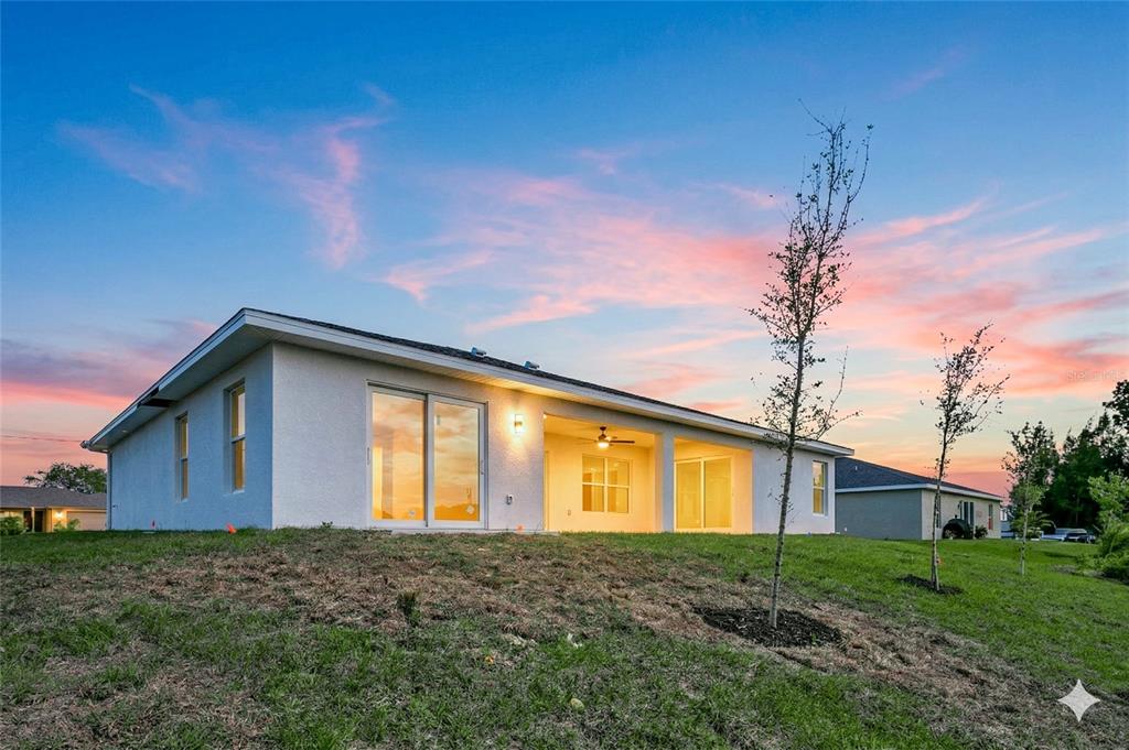The rear exterior of a single-story white house features a covered patio and sliding doors — 2210 NW 2ND AVENUE, CAPE CORAL, FL
