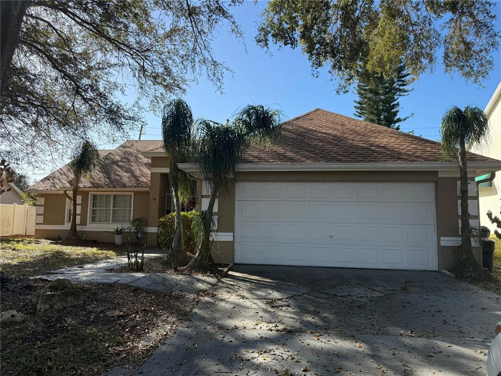 A single-story house with a tan exterior, a two-car garage, and palm trees in front — 7736 ROLLINGRIDGE COURT, ORLANDO, FL