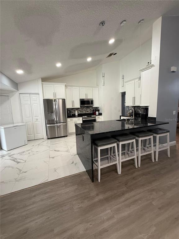 A kitchen features white cabinets, black granite countertops, a large island, and marble-look tile flooring — 7736 ROLLINGRIDGE COURT, ORLANDO, FL