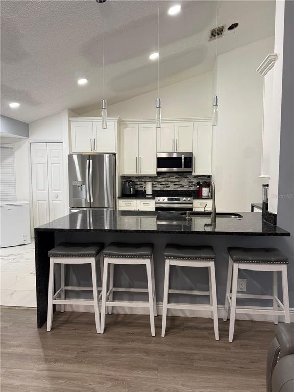 A kitchen features a dark granite island with four stools, white cabinets, and stainless appliances — 7736 ROLLINGRIDGE COURT, ORLANDO, FL