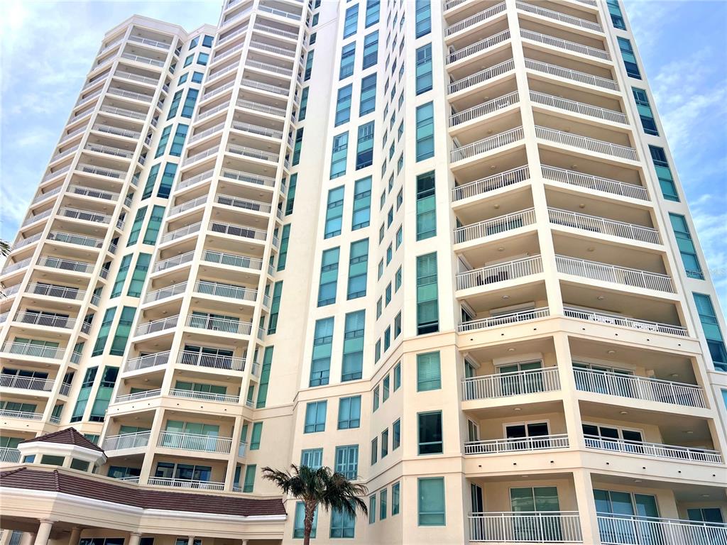 A low-angle view of a tall, beige residential high-rise building with many balconies and windows — 1180 GULF BLVD UNIT 306, CLEARWATER, FL