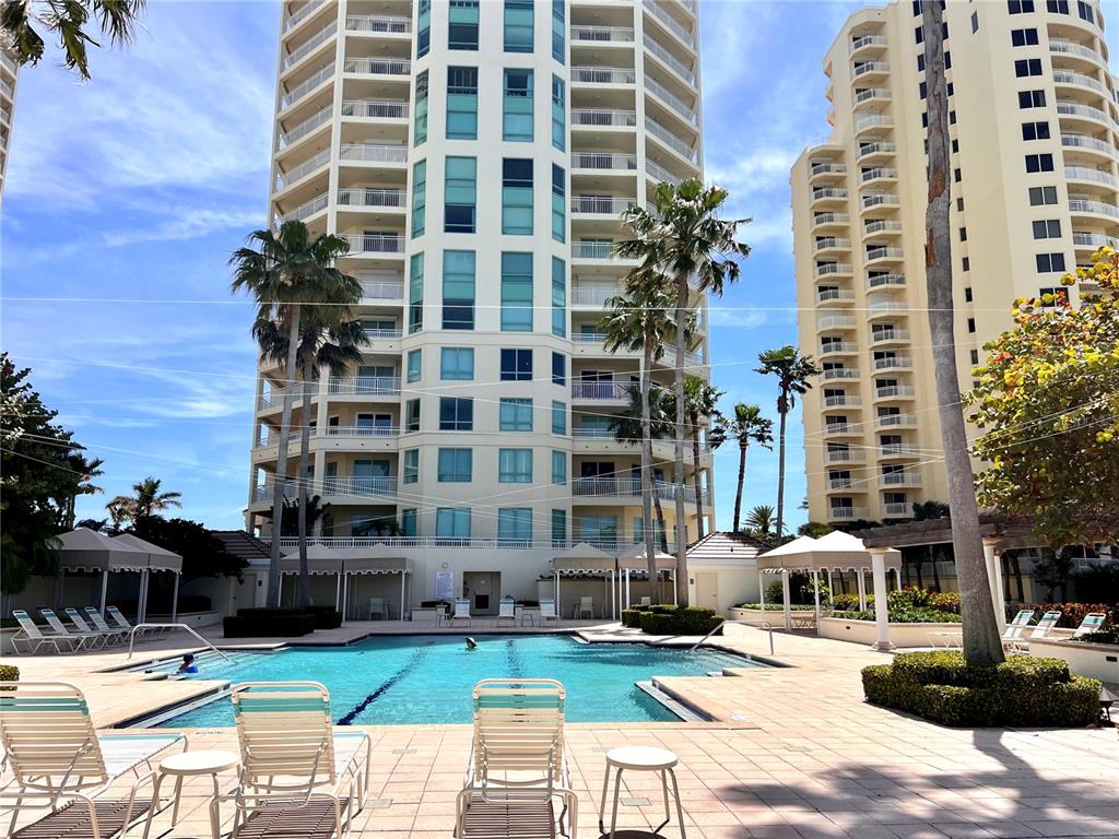 A swimming pool sits in front of two tall residential buildings under a blue sky — 1180 GULF BLVD UNIT 306, CLEARWATER, FL