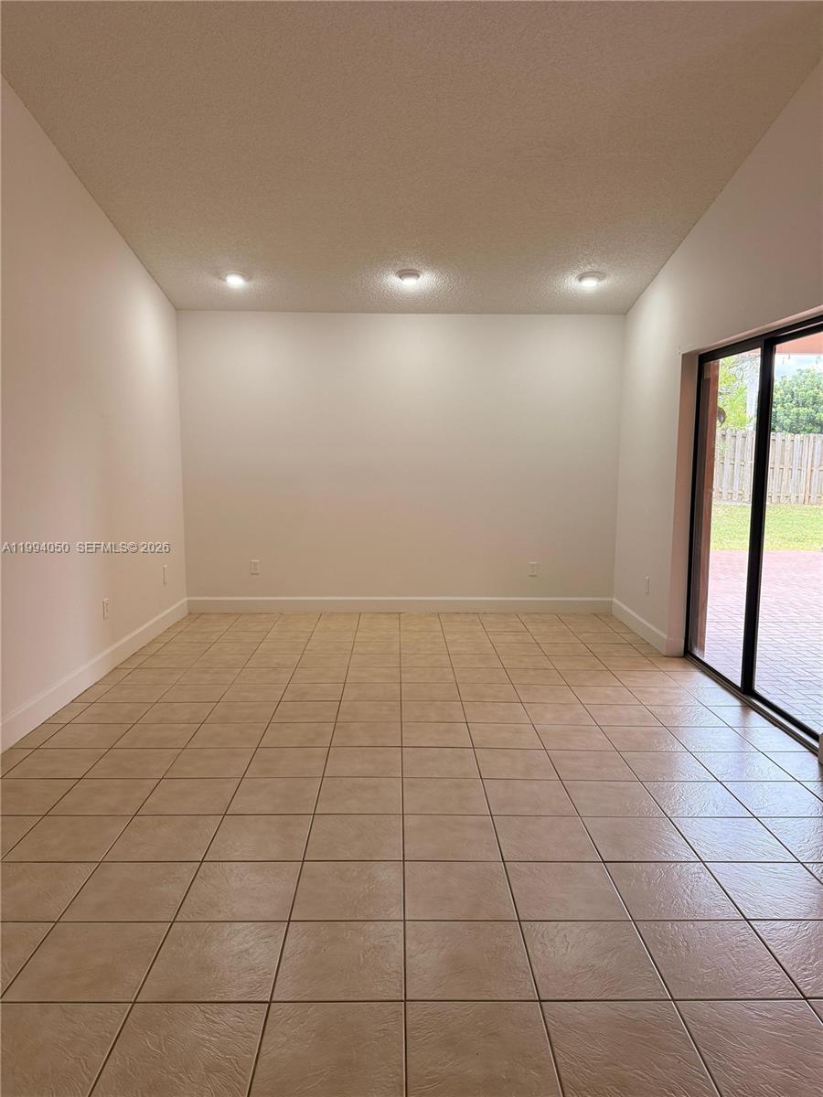 An empty room features beige tile flooring, white walls, recessed lighting, and a sliding glass door — 14729 SW 53rd Ter, Miami FL 33185, MIAMI, FL