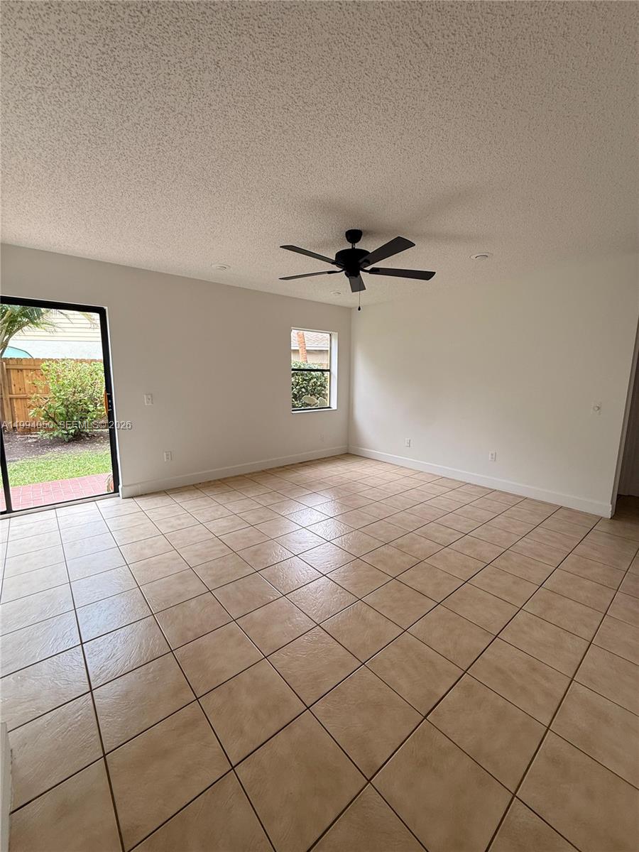 An empty room features beige tile flooring, white walls, a ceiling fan, and a sliding door — 14729 SW 53rd Ter, Miami FL 33185, MIAMI, FL