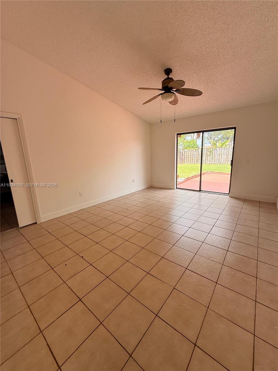 An empty room features beige tile flooring, a vaulted ceiling, and a sliding glass door — 14729 SW 53rd Ter, Miami FL 33185, MIAMI, FL