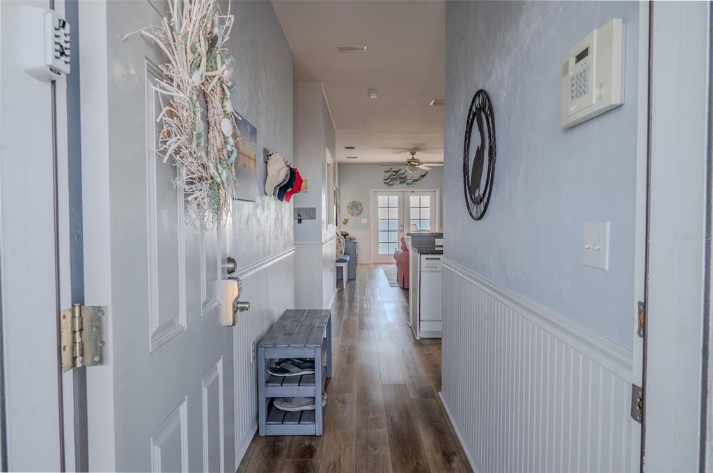 A hallway with wood-look flooring, beadboard wainscoting, and a bench leads toward a living area — 502 MAIN STREET UNIT 207, HORSESHOE BEACH, FL