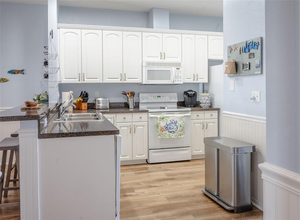 A kitchen features white cabinets, granite countertops, stainless steel appliances, and light wood flooring — 502 MAIN STREET UNIT 207, HORSESHOE BEACH, FL