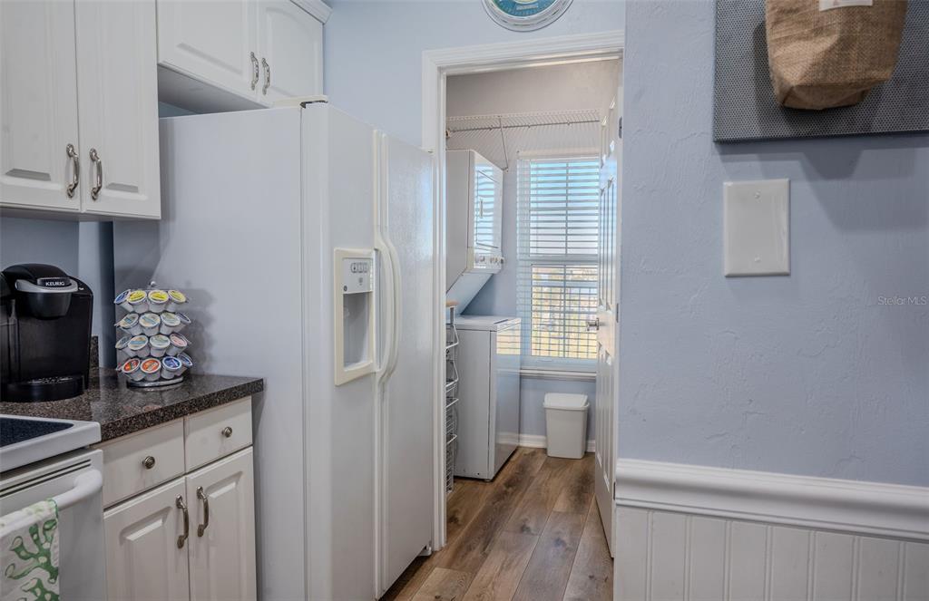 A kitchen with white cabinets and a refrigerator leads into a laundry room with appliances — 502 MAIN STREET UNIT 207, HORSESHOE BEACH, FL