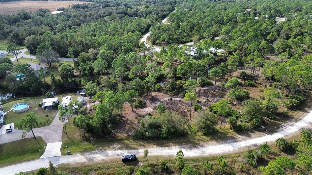 An aerial view shows a wooded lot with a gravel road, trailers, and a pool — 13599 CAROUSEL DRIVE, PUNTA GORDA, FL
