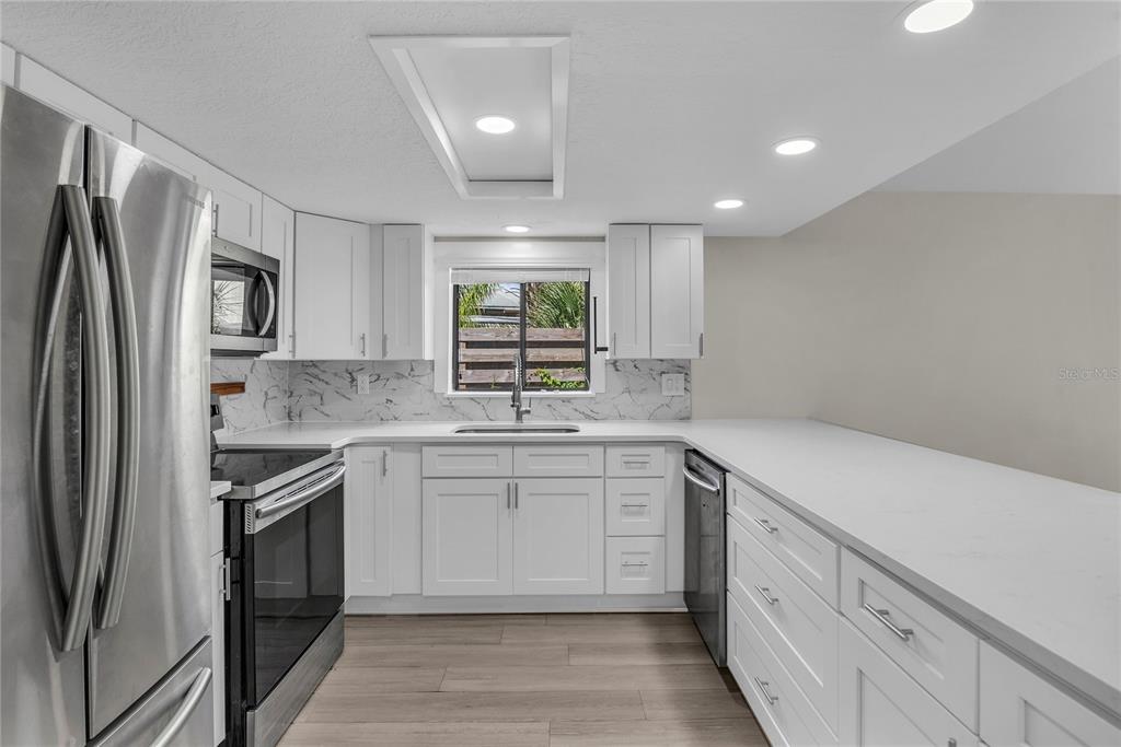 A modern kitchen features white cabinets, stainless steel appliances, marble-patterned backsplash, and light wood flooring — 189 OAK LANE, FLAGLER BEACH, FL
