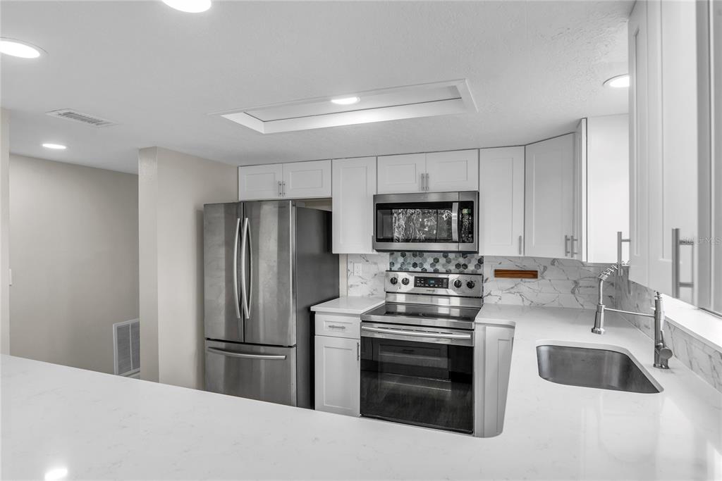 A kitchen features white cabinets, stainless steel appliances, a marble-look backsplash, and white countertops — 189 OAK LANE, FLAGLER BEACH, FL