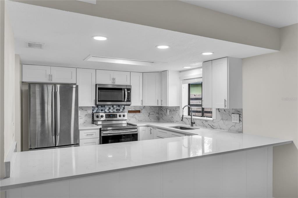 A modern kitchen features white cabinets, stainless steel appliances, and a white quartz breakfast bar — 189 OAK LANE, FLAGLER BEACH, FL