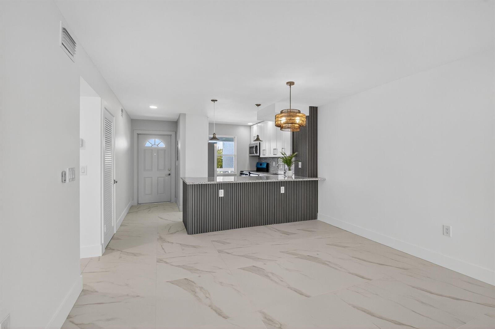 An open-concept kitchen features a gray slatted island, white cabinets, and light marble-look tile flooring — 9886 Marina Boulevard # 622, Boca Raton FL 33428, BOCA RATON, FL