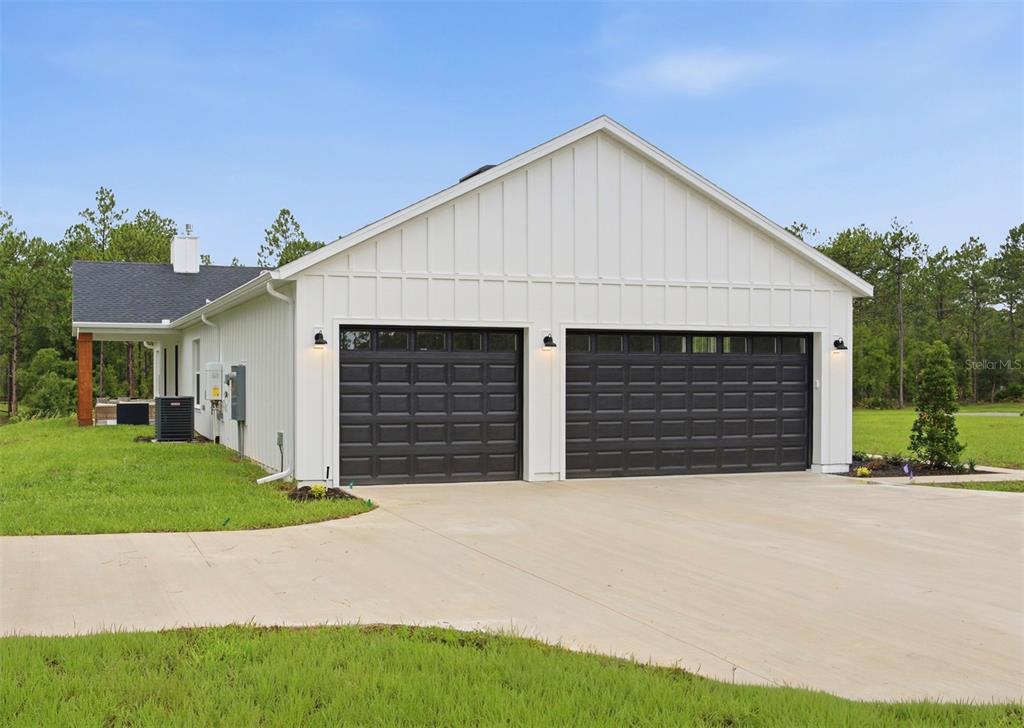 A white board-and-batten house exterior features two black garage doors and a concrete driveway — 6534 N HARCROSS AVENUE, DUNNELLON, FL
