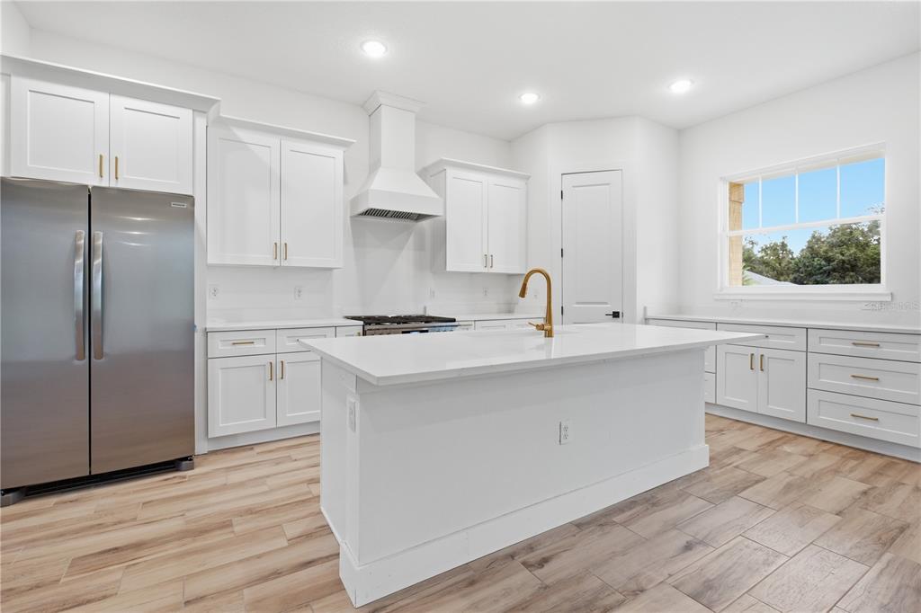 A modern kitchen features white cabinetry, stainless steel appliances, a center island, and wood-look flooring — 6534 N HARCROSS AVENUE, DUNNELLON, FL