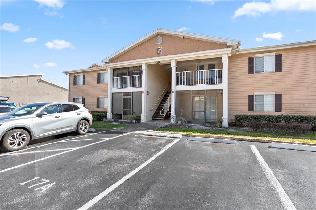 A two-story apartment building with tan siding, screened balconies, and a parking lot in front — 145 N PEARL LAKE CAUSEWAY UNIT 106, ALTAMONTE SPRINGS, FL
