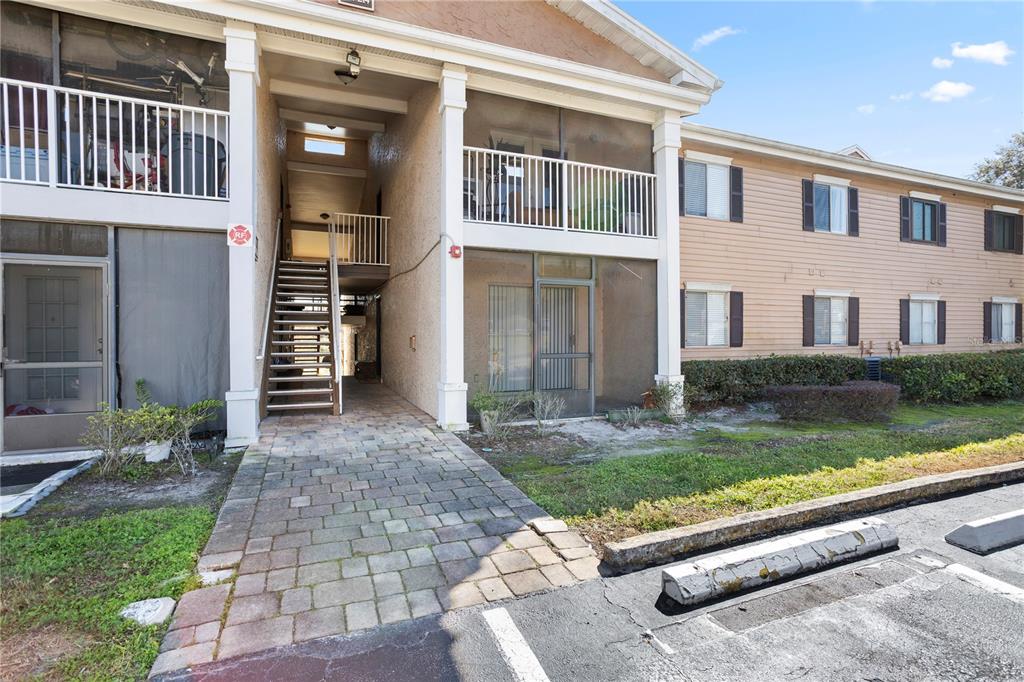 A two-story apartment building exterior features a paved walkway leading to a central staircase — 145 N PEARL LAKE CAUSEWAY UNIT 106, ALTAMONTE SPRINGS, FL