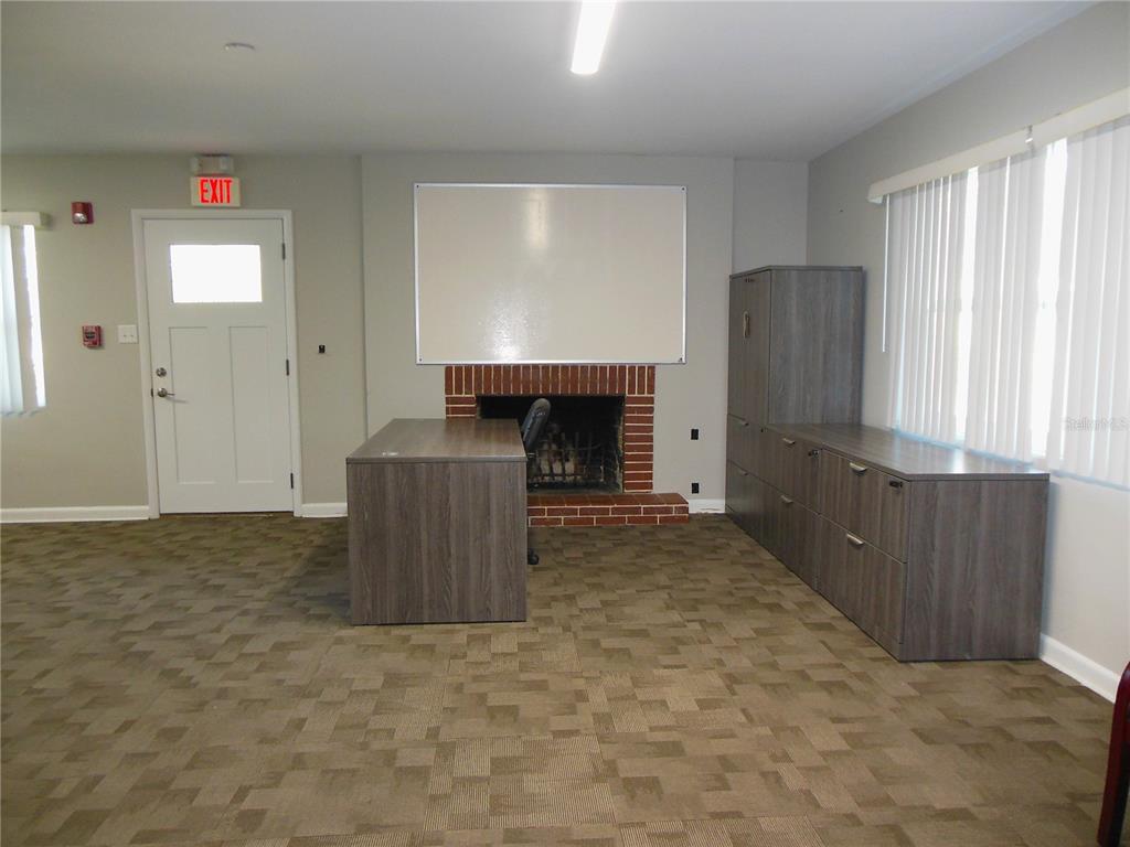 An office space features a brick fireplace, a desk, storage cabinets, and carpeted flooring — 500 S DEXTER AVENUE, DELAND, FL