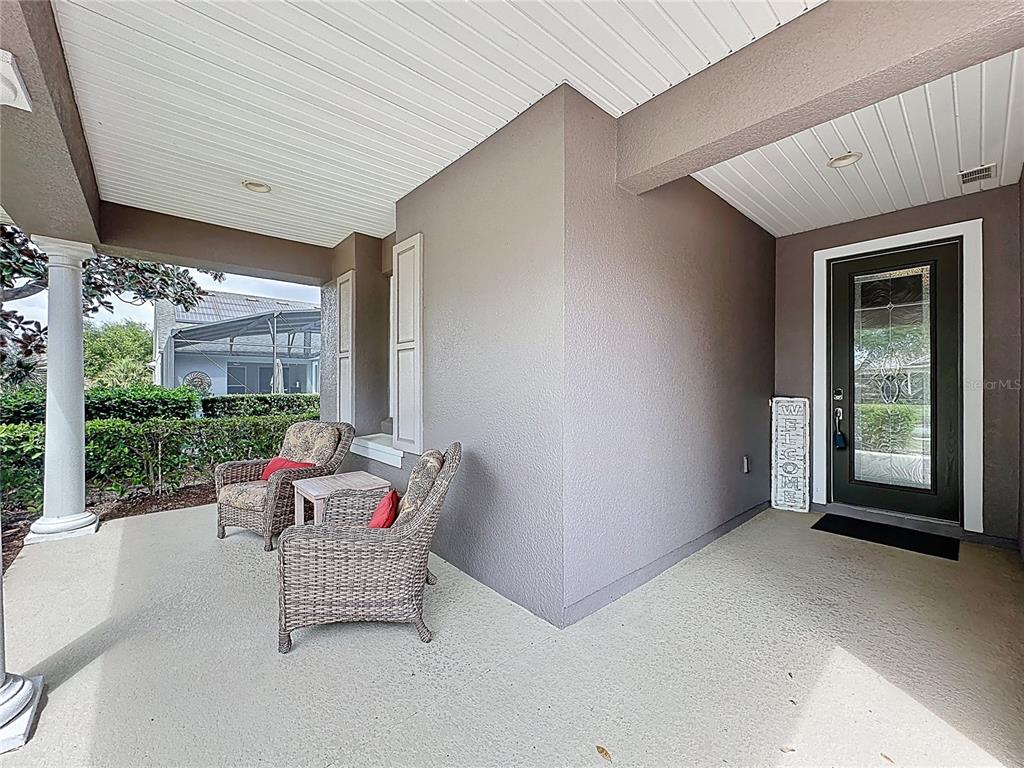 A covered front porch features two wicker chairs, a small table, and a glass-paneled door — 108 MIST FLOWER LANE, GROVELAND, FL