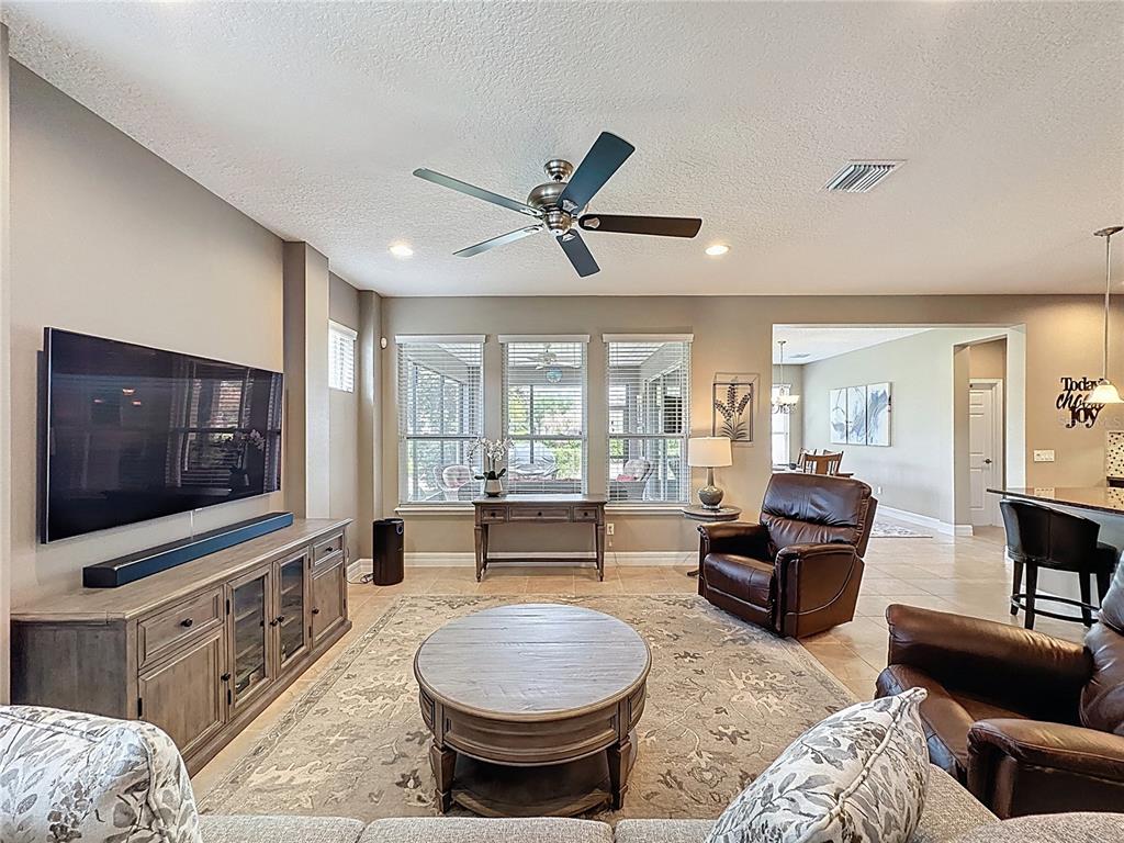 A living room features a large television, leather armchairs, a round coffee table, and windows — 108 MIST FLOWER LANE, GROVELAND, FL