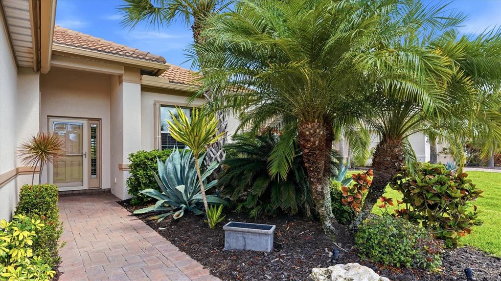 A paved walkway leads to the front entrance of a house with tropical landscaping — 13177 CREEKSIDE LANE, PORT CHARLOTTE, FL