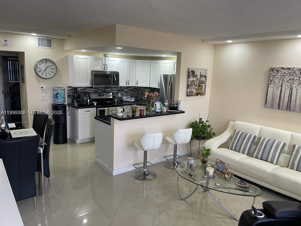 An open-concept kitchen with white cabinets and a breakfast bar overlooks a living area — 3200 NE 7th Ct # 306C, Pompano Beach FL 33062, POMPANO BEACH, FL