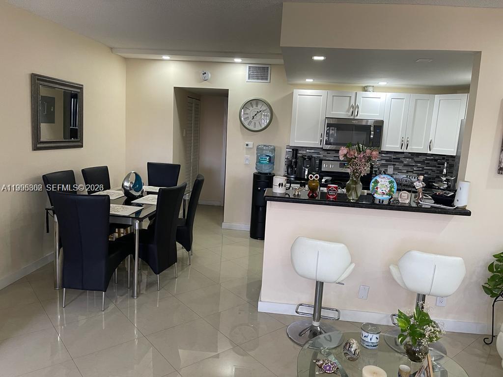 An open-concept dining area and kitchen feature white cabinets, a breakfast bar, and tile flooring — 3200 NE 7th Ct # 306C, Pompano Beach FL 33062, POMPANO BEACH, FL