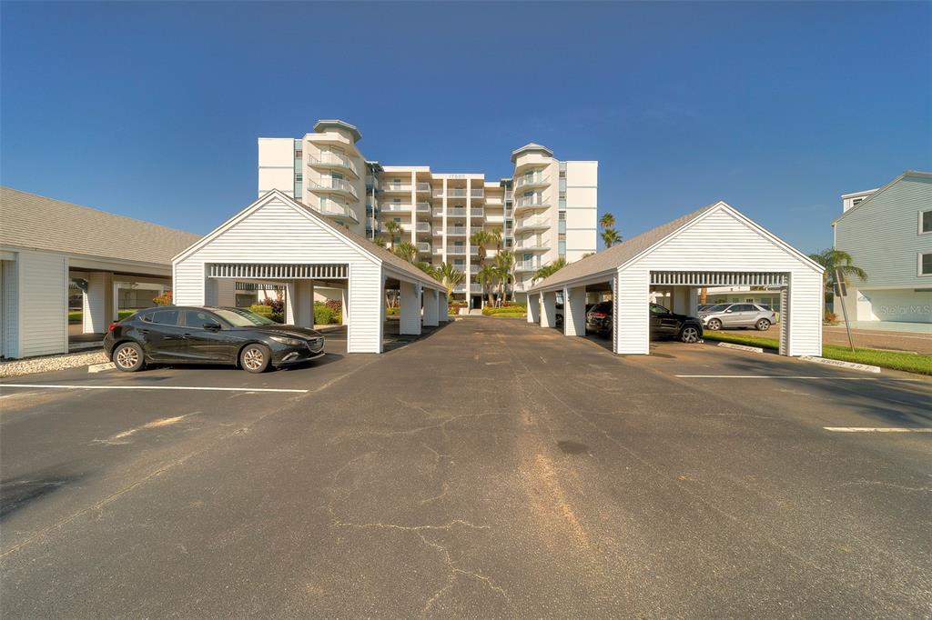 A multi-story apartment building stands behind two rows of covered parking spaces — 17980 GULF BOULEVARD UNIT 402, REDINGTON SHORES, FL