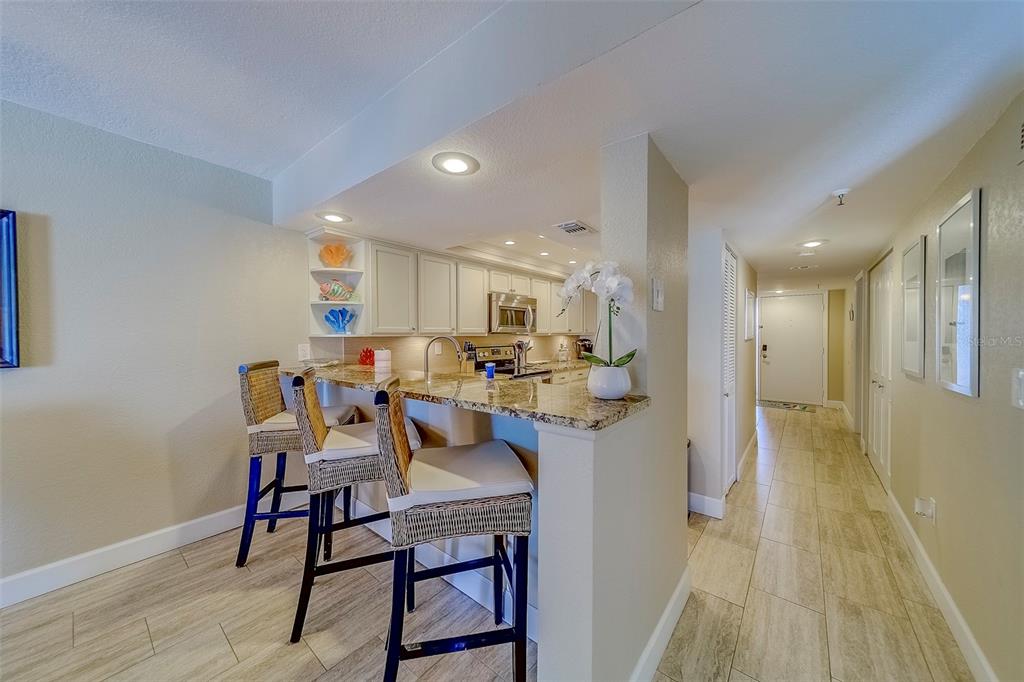 A kitchen with granite countertops and a breakfast bar with three wicker stools — 17980 GULF BOULEVARD UNIT 402, REDINGTON SHORES, FL