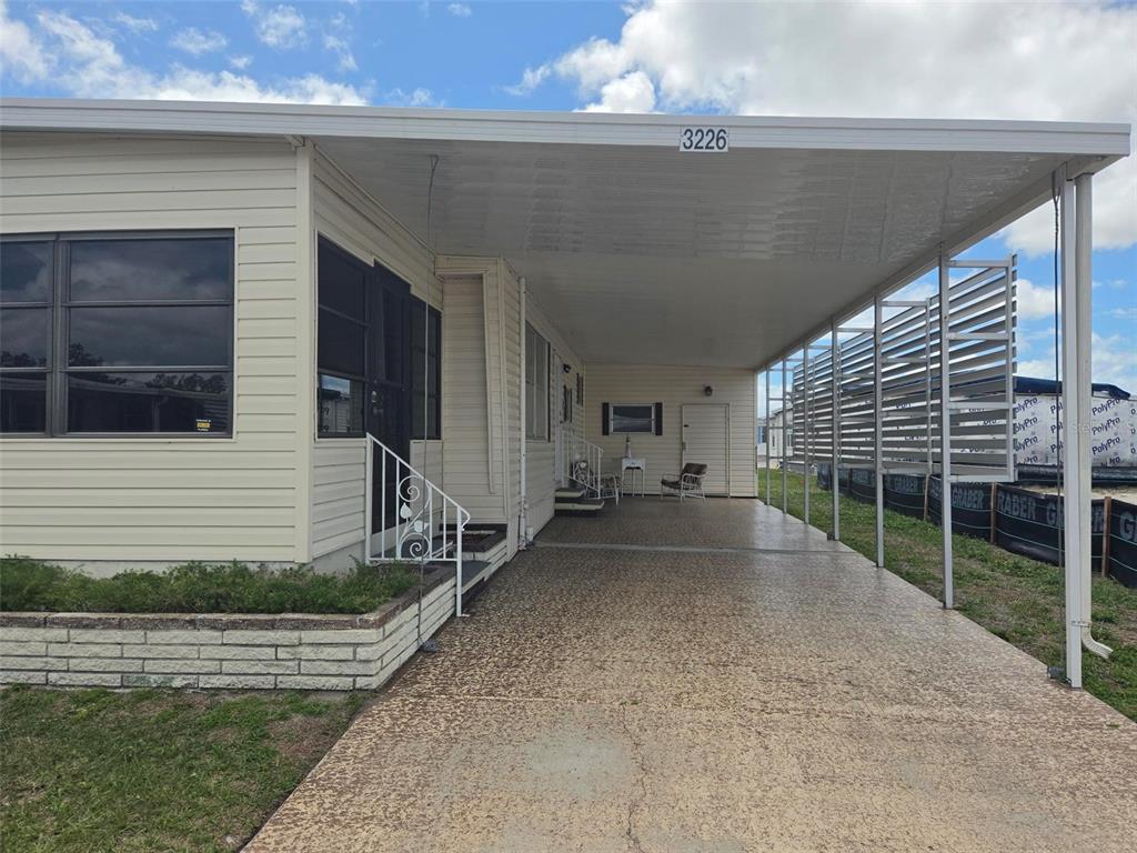 A mobile home exterior features a long covered carport, a concrete driveway, and white siding — 3226 SWEET GUM TERRACE, SARASOTA, FL