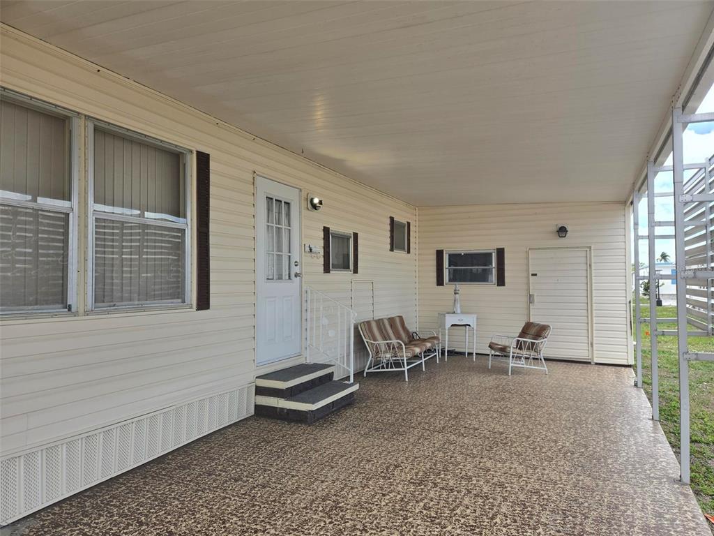 A covered patio with light siding, a white door, and outdoor furniture on a concrete floor — 3226 SWEET GUM TERRACE, SARASOTA, FL