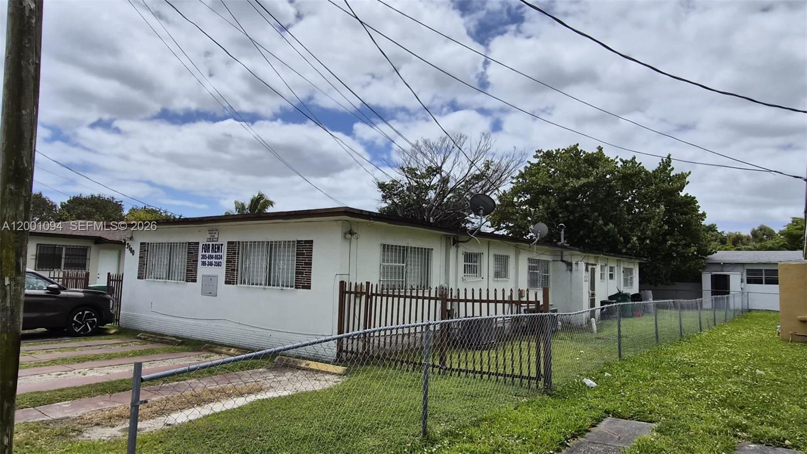 A single-story white building with security bars on windows sits behind a chain-link fence — 3180 NW 19th Ave, Miami FL 33142, MIAMI, FL