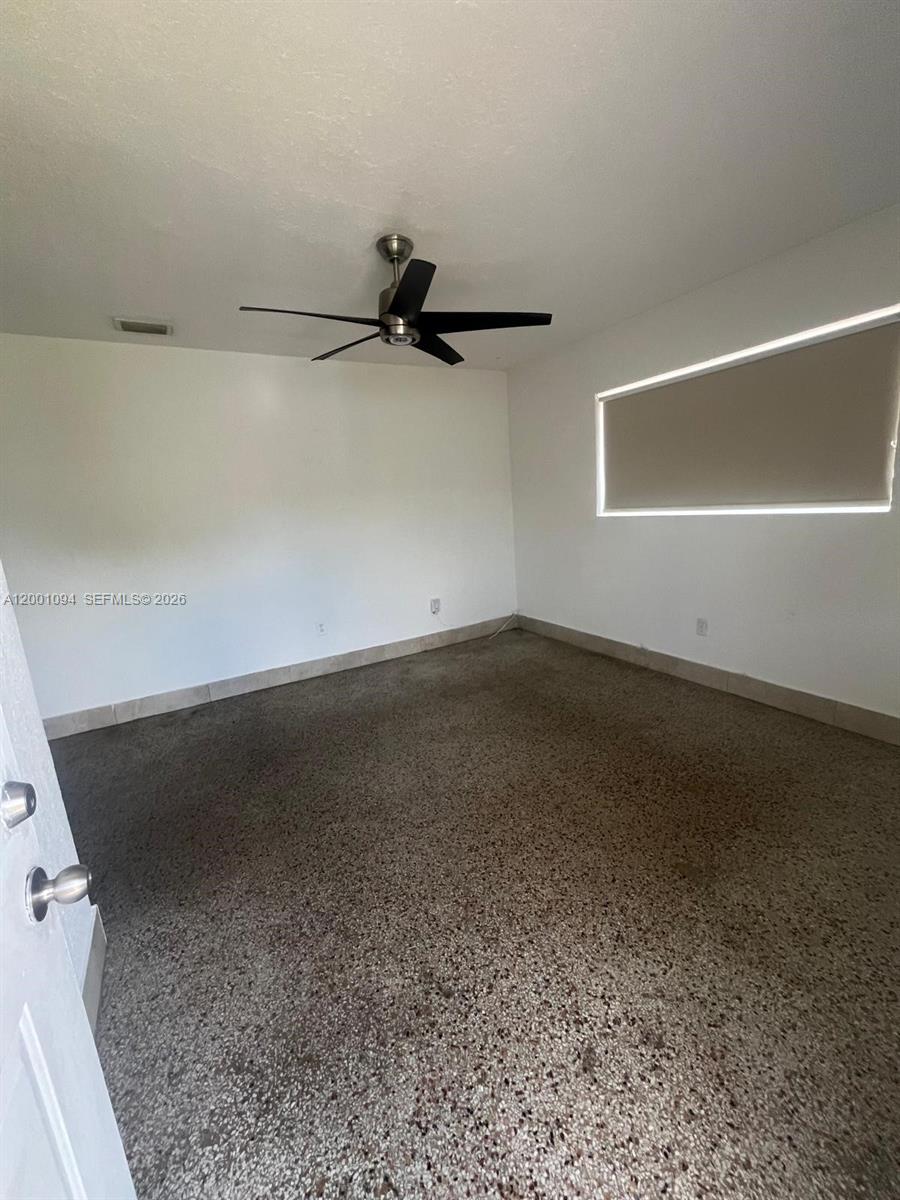 A bedroom features white walls, a ceiling fan, and speckled flooring with a baseboard trim — 3180 NW 19th Ave, Miami FL 33142, MIAMI, FL