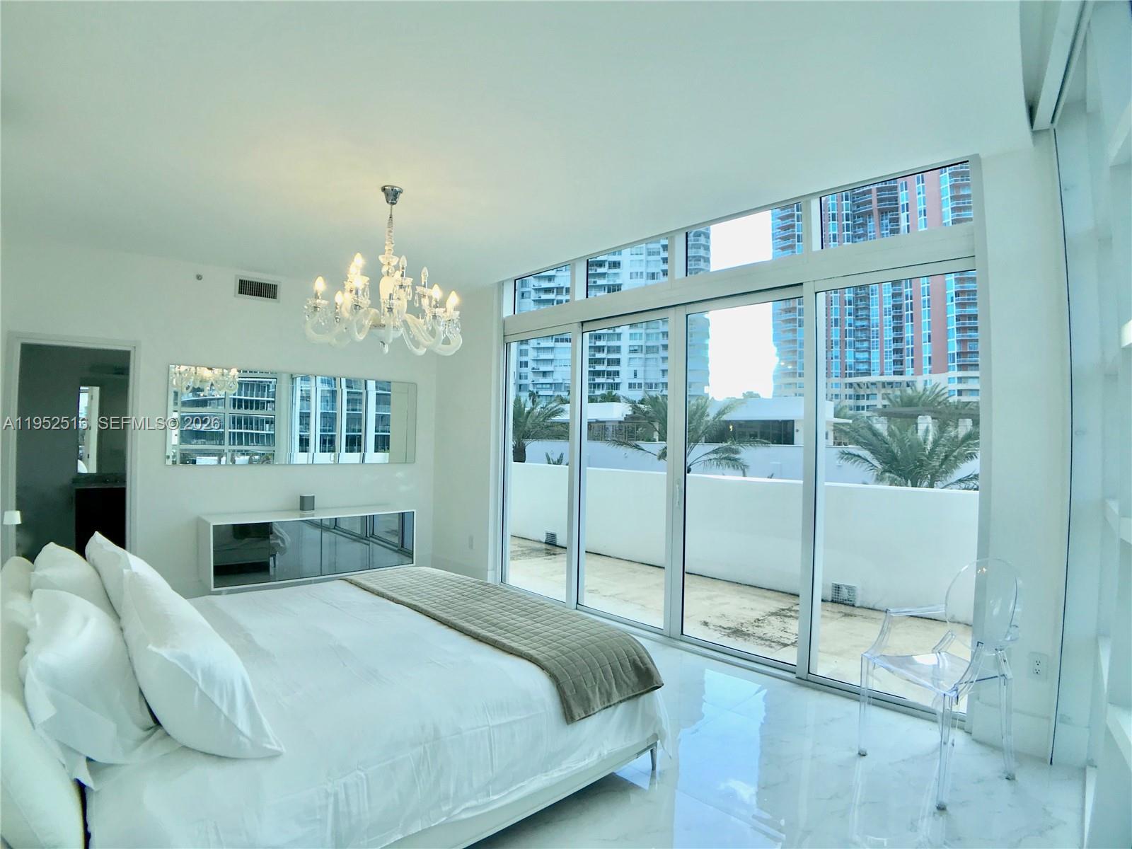 A bright bedroom features white marble floors, a crystal chandelier, and floor-to-ceiling windows overlooking buildings — 50 S Pointe Dr, Miami Beach FL 33139, MIAMI BEACH, FL