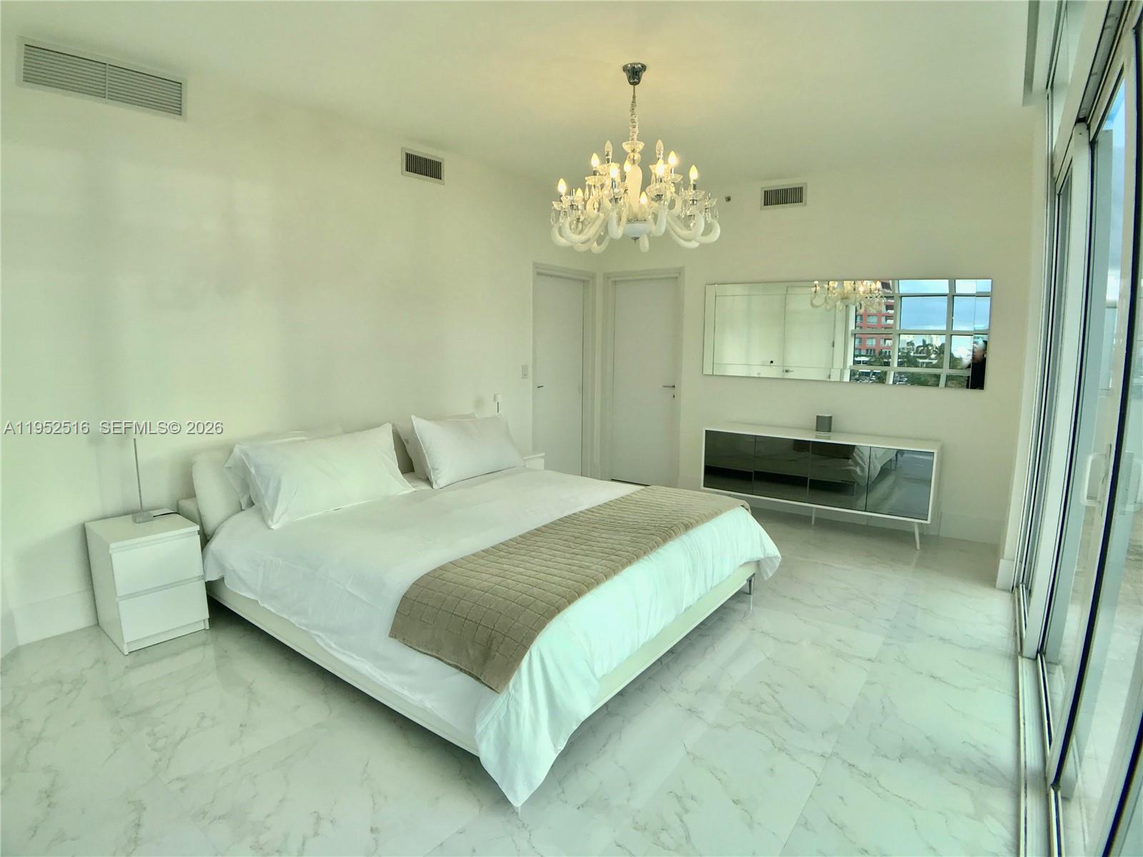 A bright bedroom features a white bed, a crystal chandelier, and marble flooring — 50 S Pointe Dr, Miami Beach FL 33139, MIAMI BEACH, FL